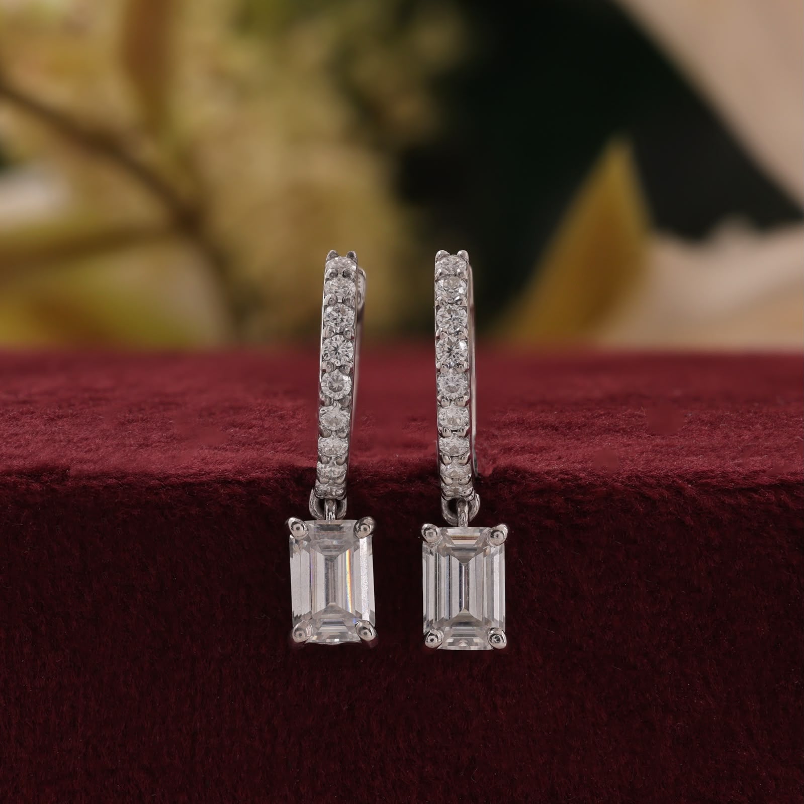 White gold sparkling pavé-set round accent diamonds on the hoops and suspended emerald-cut diamond center stones.