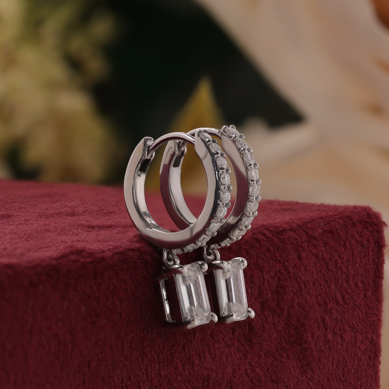 White gold sparkling pavé-set round accent diamonds on the hoops and suspended emerald-cut diamond center stones.