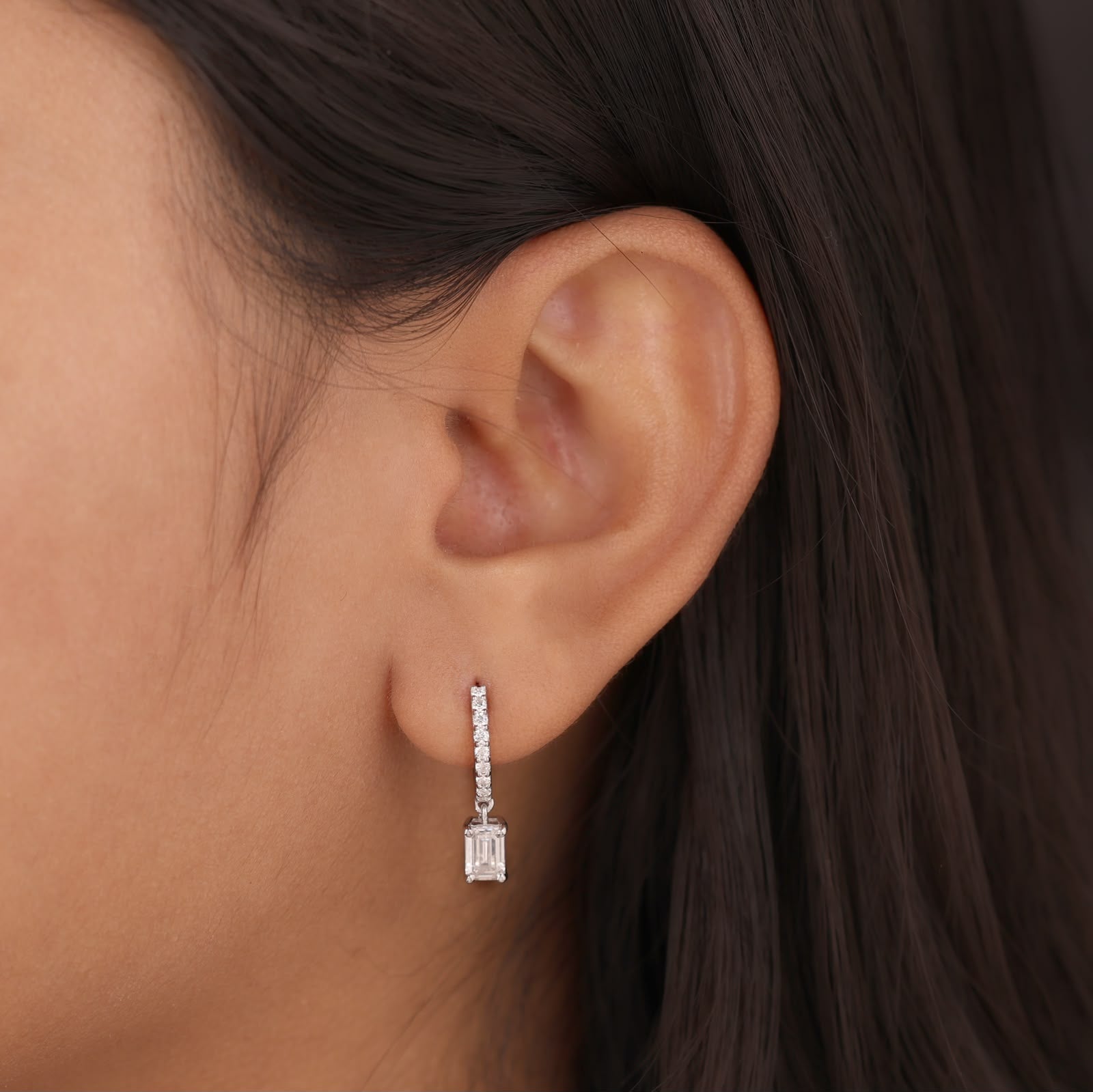 White gold sparkling pavé-set round accent diamonds on the hoops and suspended emerald-cut diamond center stones.